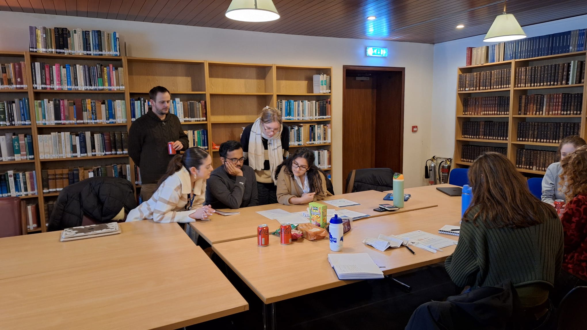 Students huddle in groups over notebooks. Snacks sit on the table.